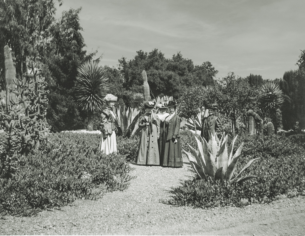 Black and white photo of women in long dresses and coats in the cactus garden