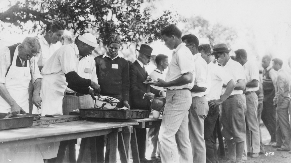 Sam McDonald serving barbecue to line of men 