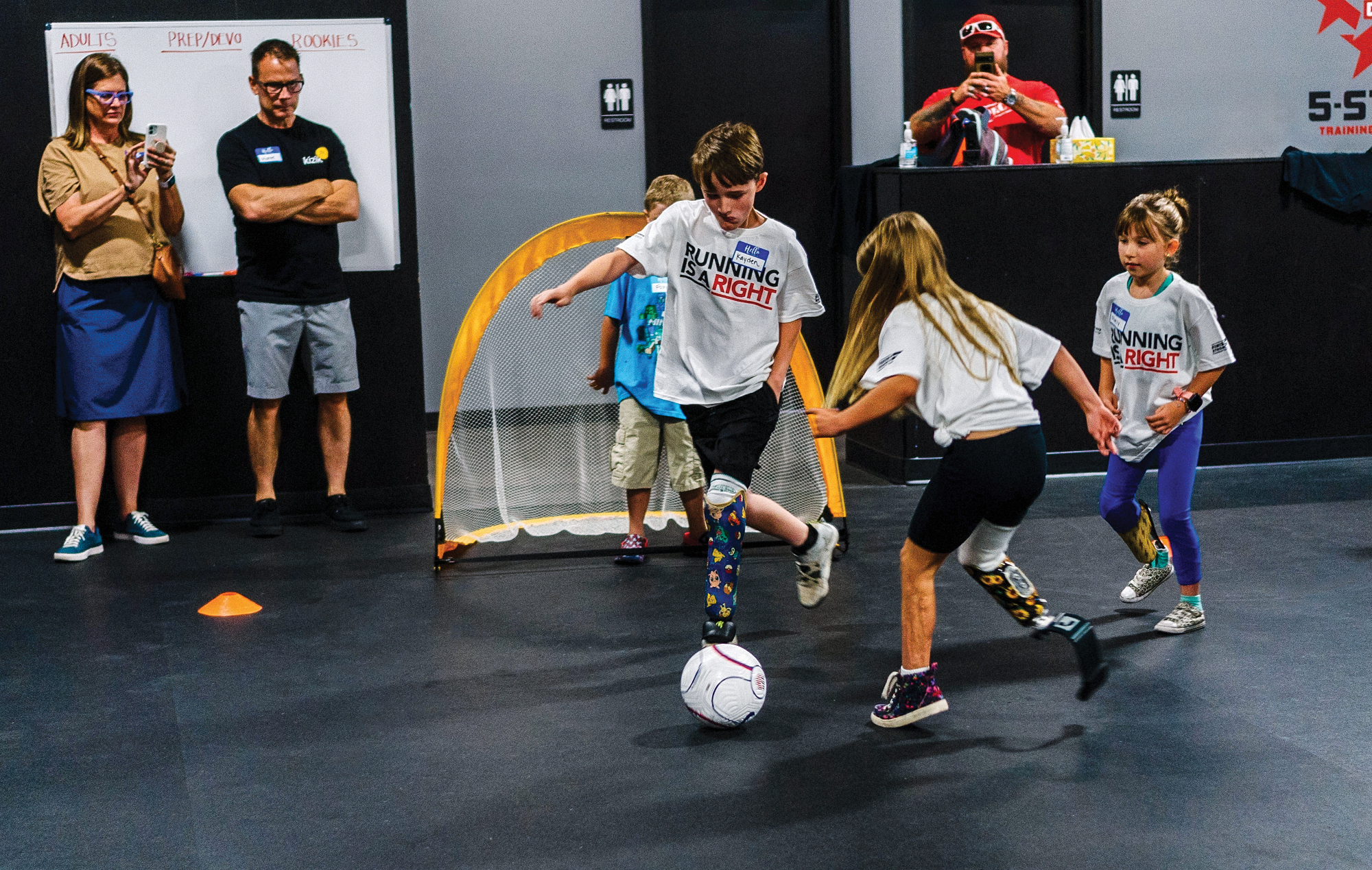 Kids playing indoor soccer with adults in the background.