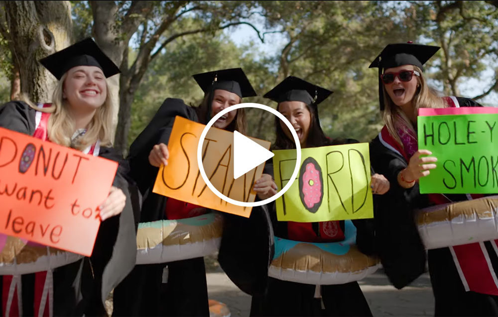 Four graduates in cap and gown holding signs