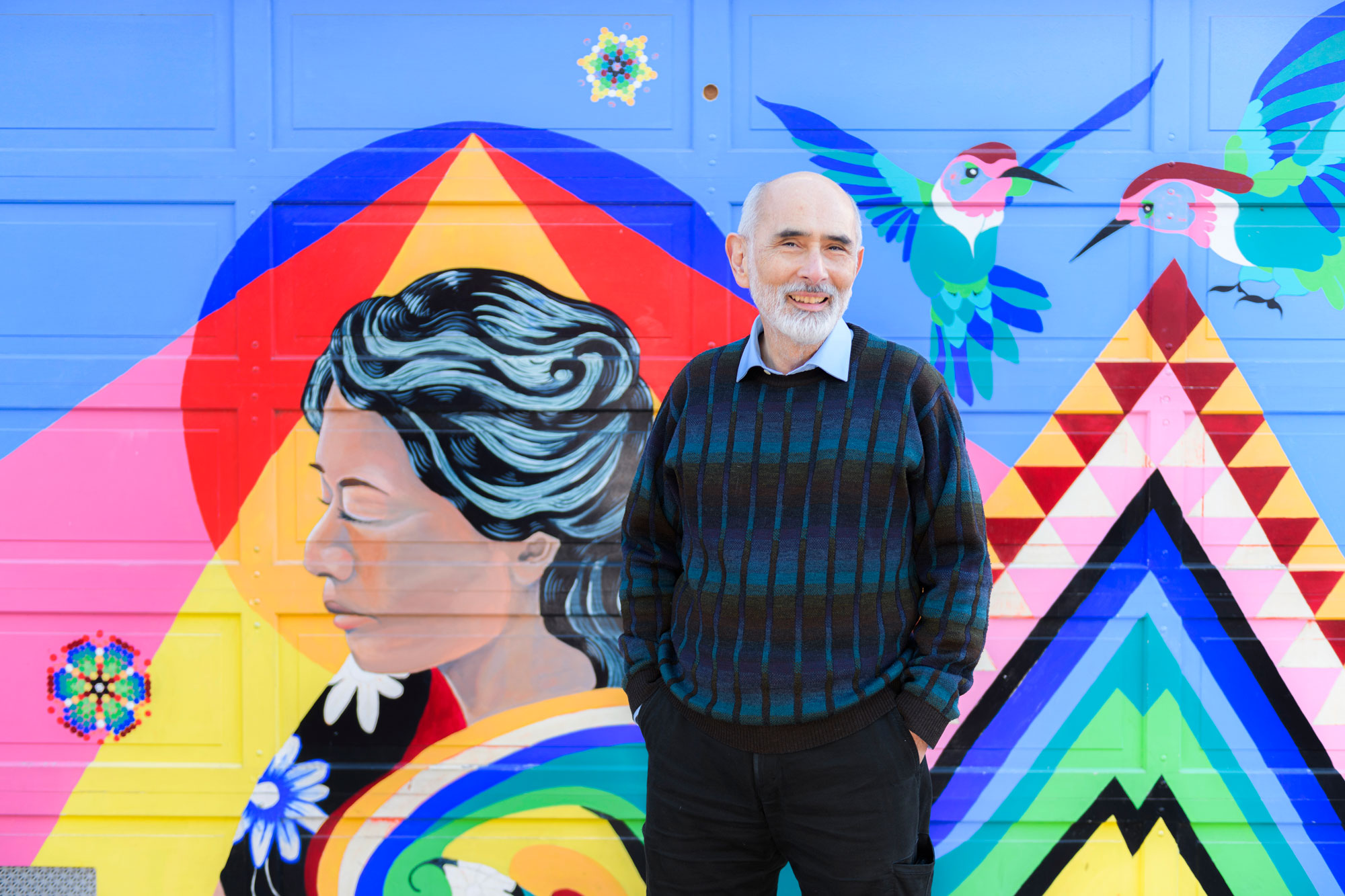 Portrait of Ricardo Muñoz standing in front of a colorful mural