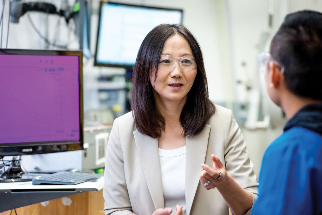 Bao, wearing safety glasses, speaks with a colleague.
