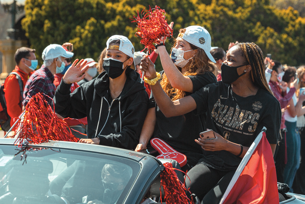 Women's basketball player in masks riding in convertible