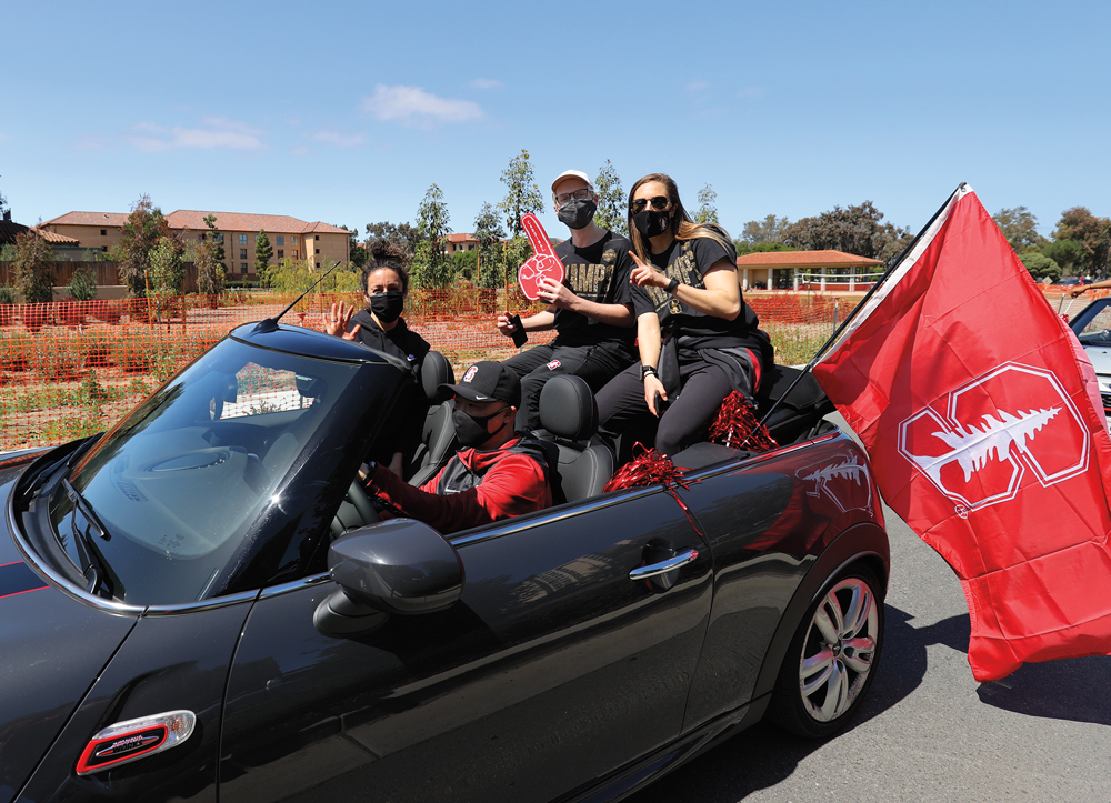 People in masks riding in convertible with Stanford flag