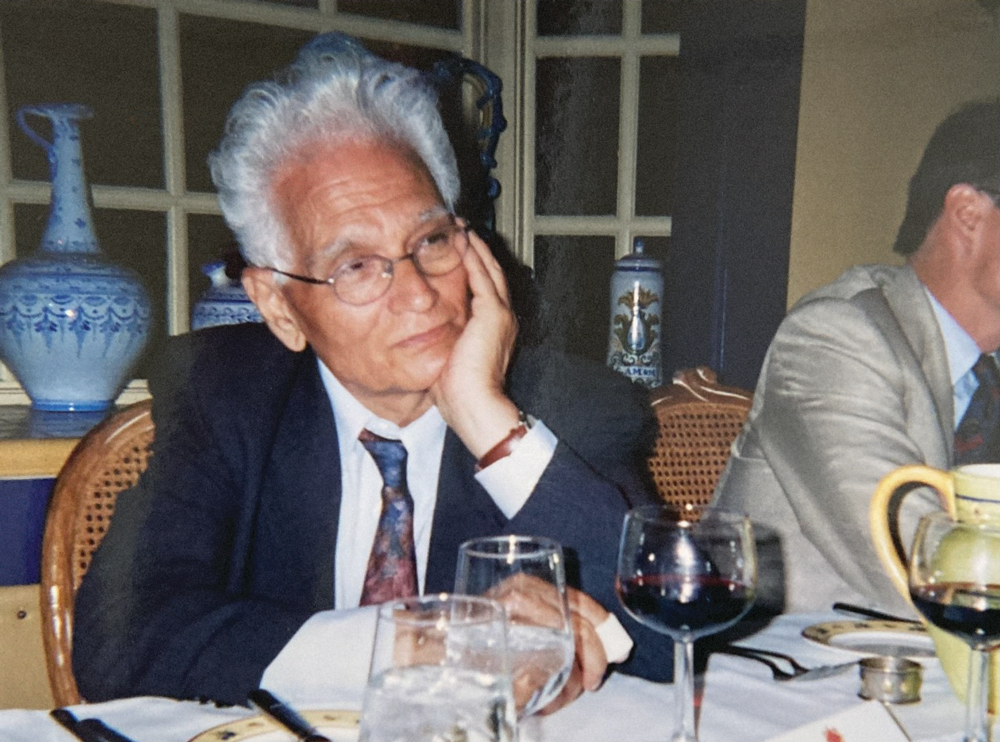 Derrida with his chin in his hand at a table in a restaurant