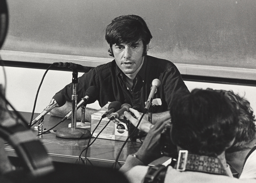Bruce Franklin sitting at a desk in front of several microphones