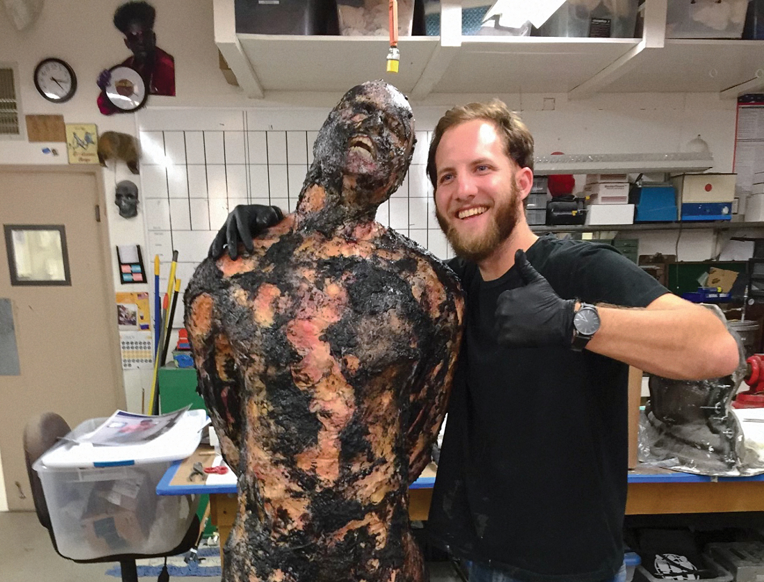 Atticus Anderson giving a thumbs up next to a charred model of a body